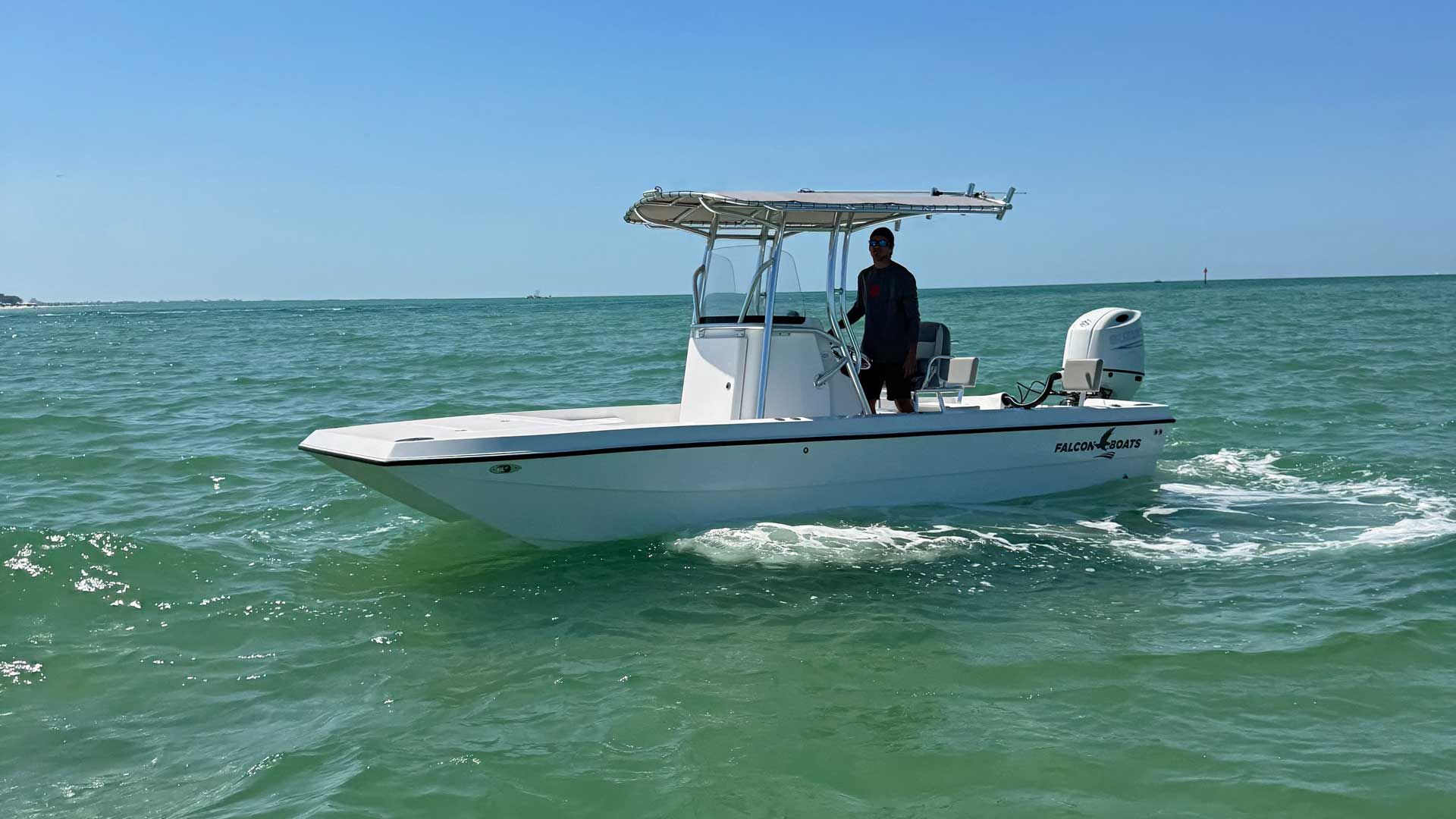A white motorboat with a person at the helm navigating through turquoise water under a bright blue sky.