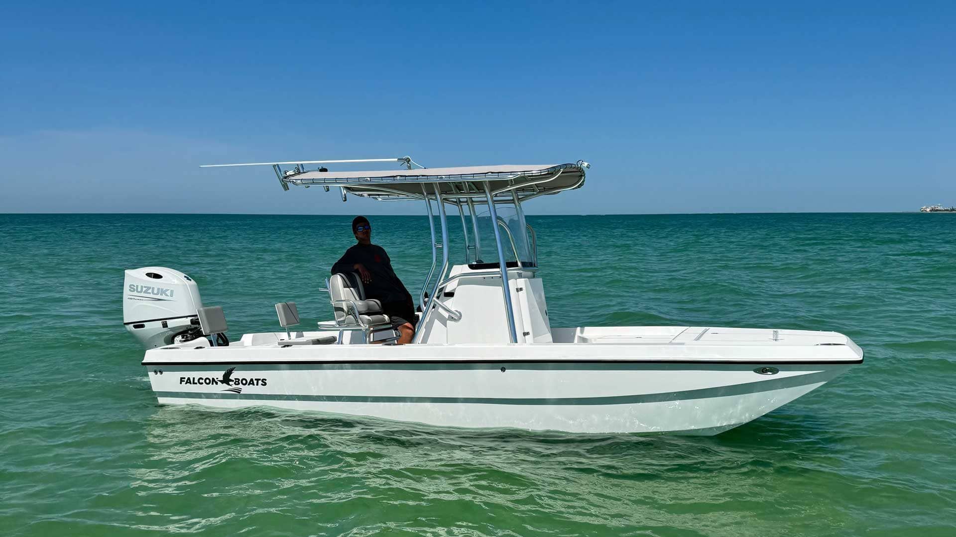 White boat with a man at the helm, on a calm turquoise ocean under a clear blue sky.