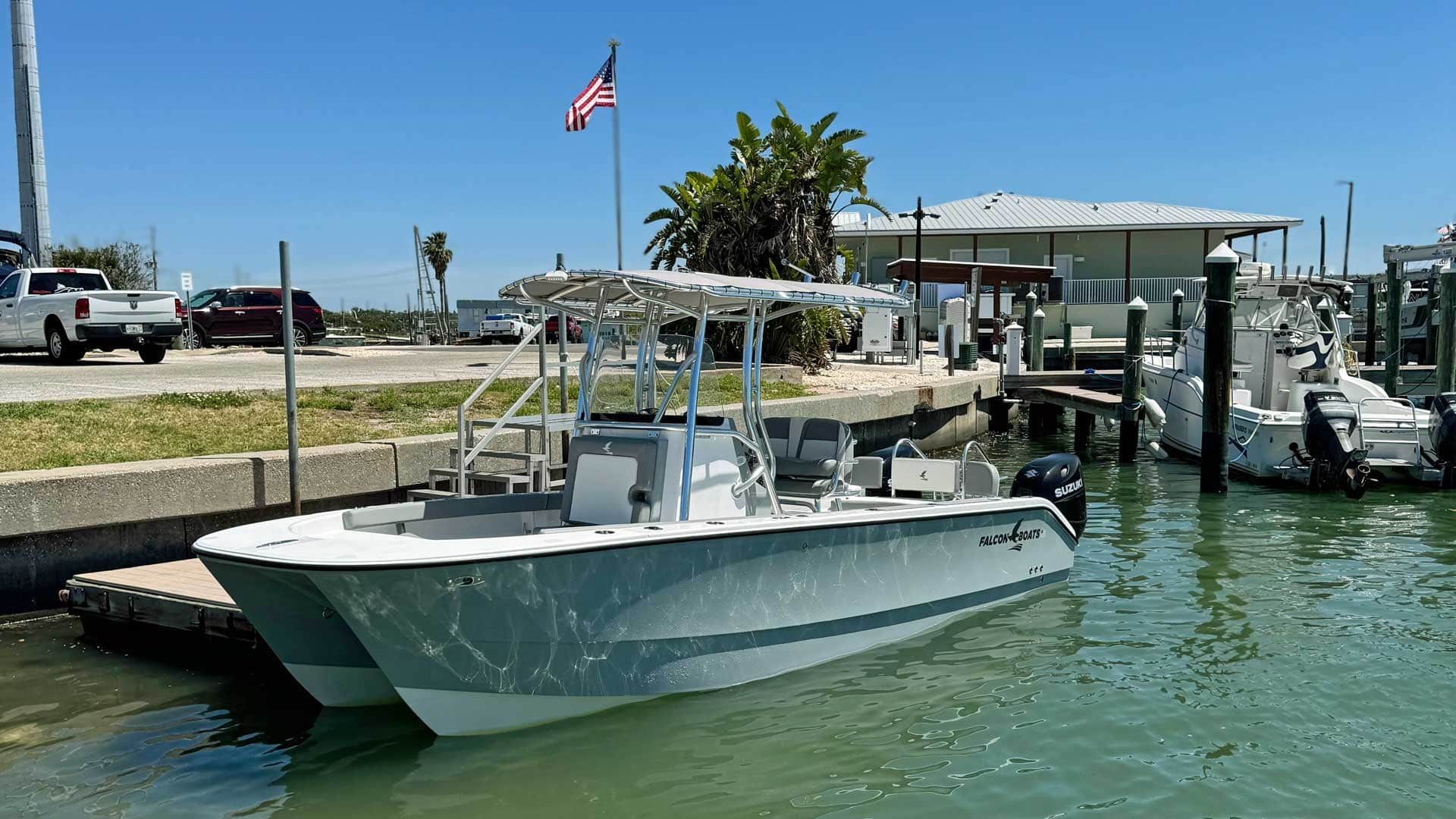 A gray catamaran boat docked near a building with an American flag on a sunny day.