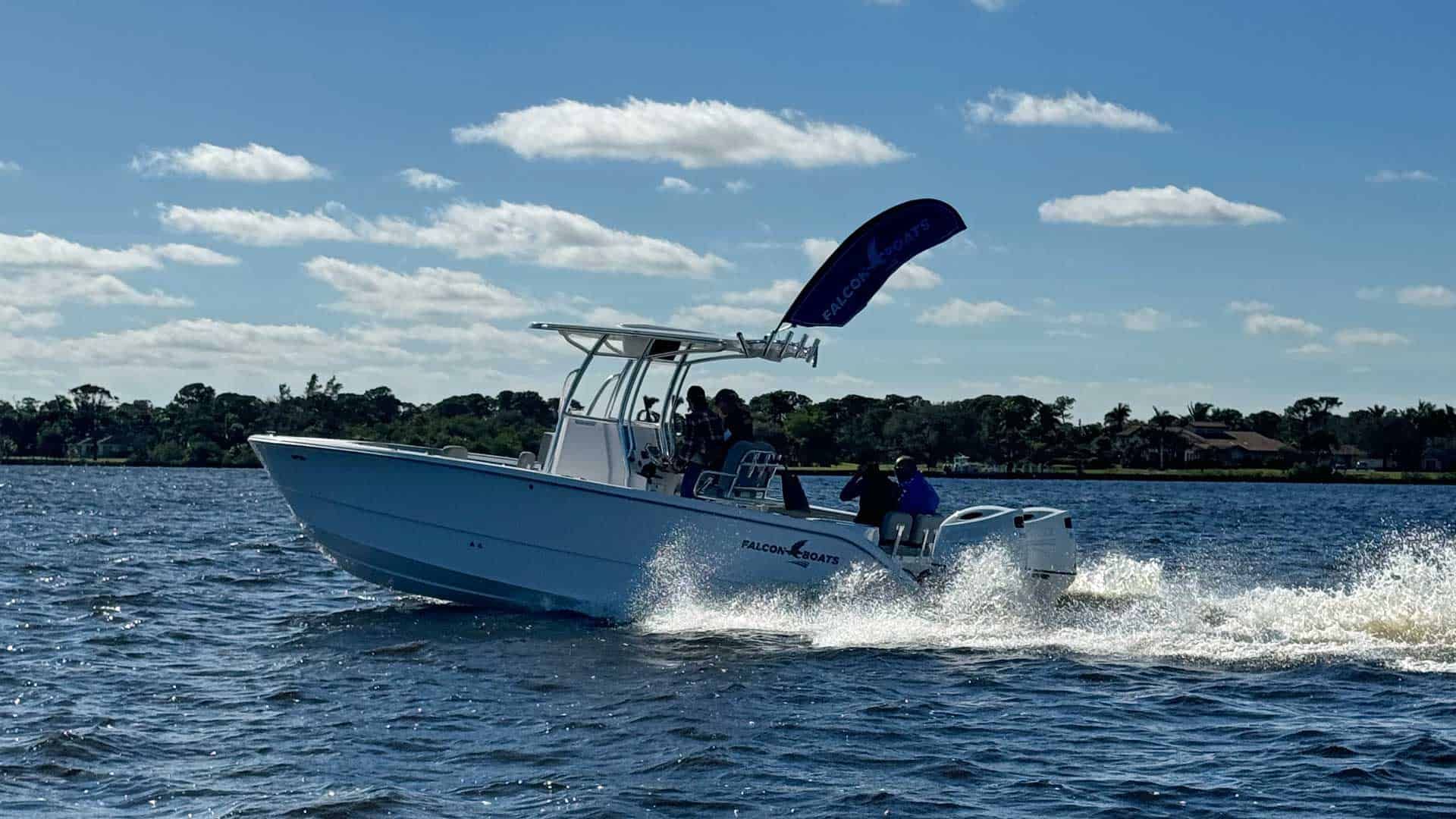 A white motorboat speeds across blue water with people on board, under a bright blue sky.