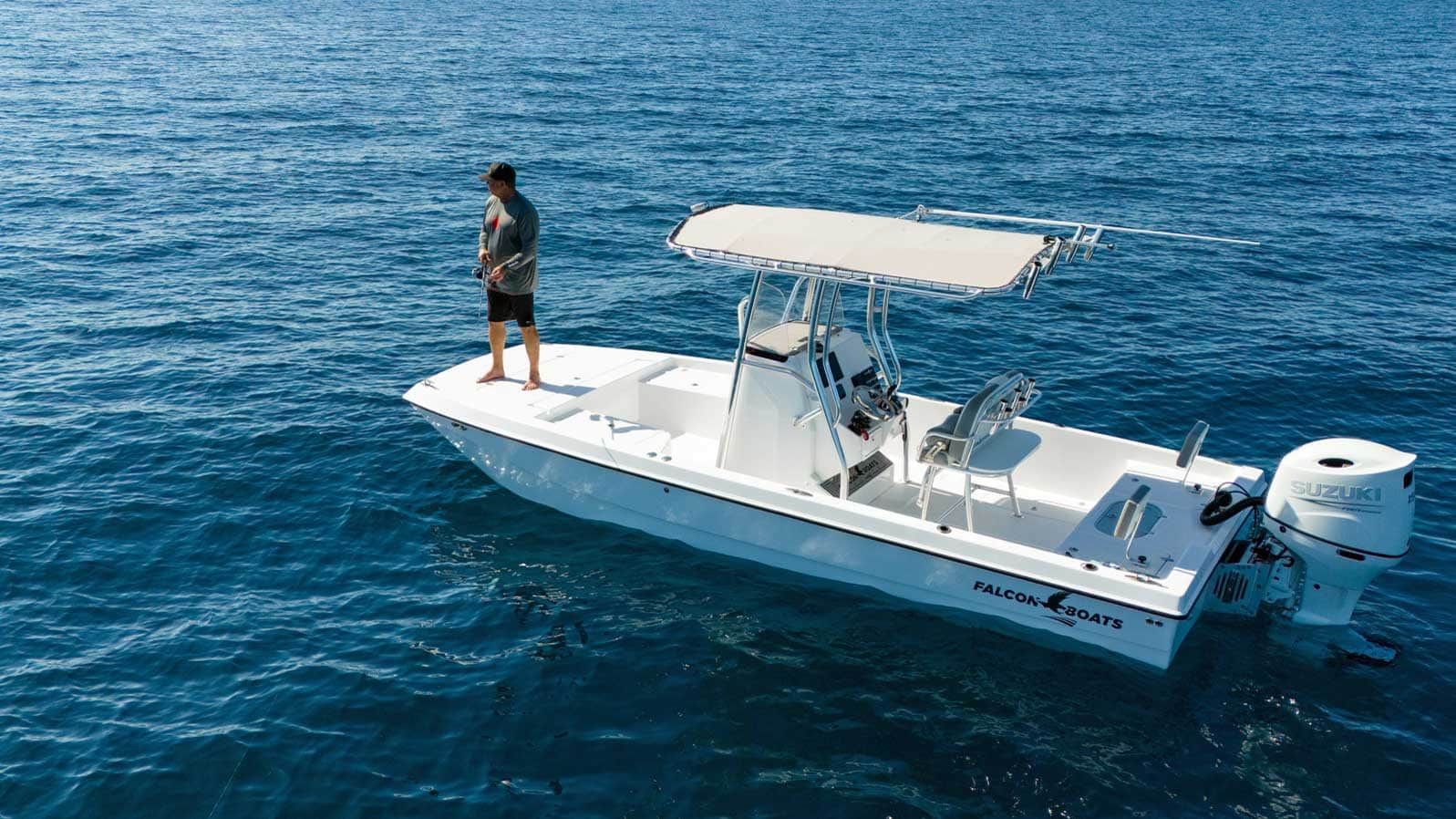 A man standing on a white fishing boat in the ocean under a bright blue sky.
