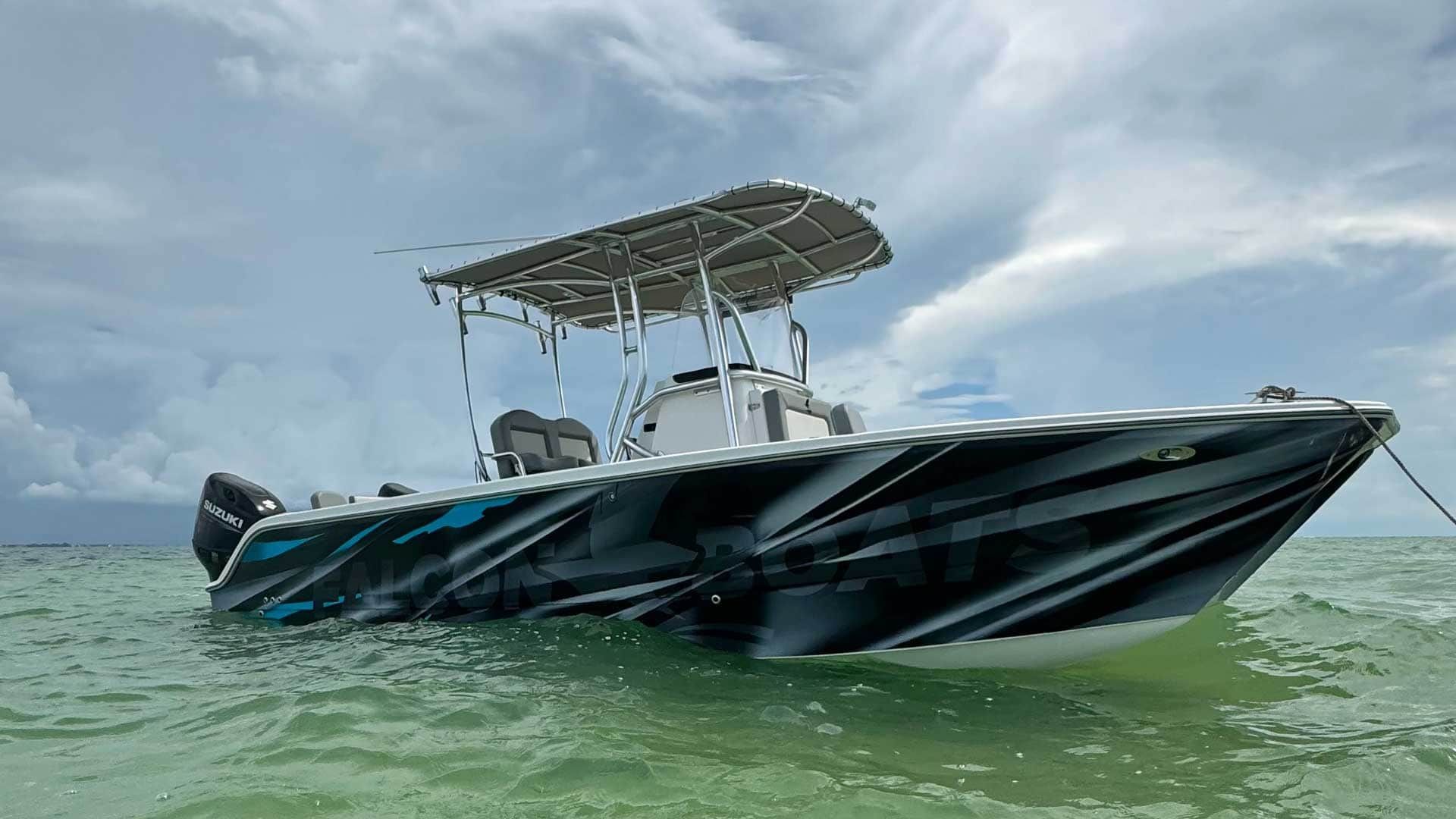 A center console boat with a black and blue patterned wrap sits in shallow, clear water under a cloudy sky.