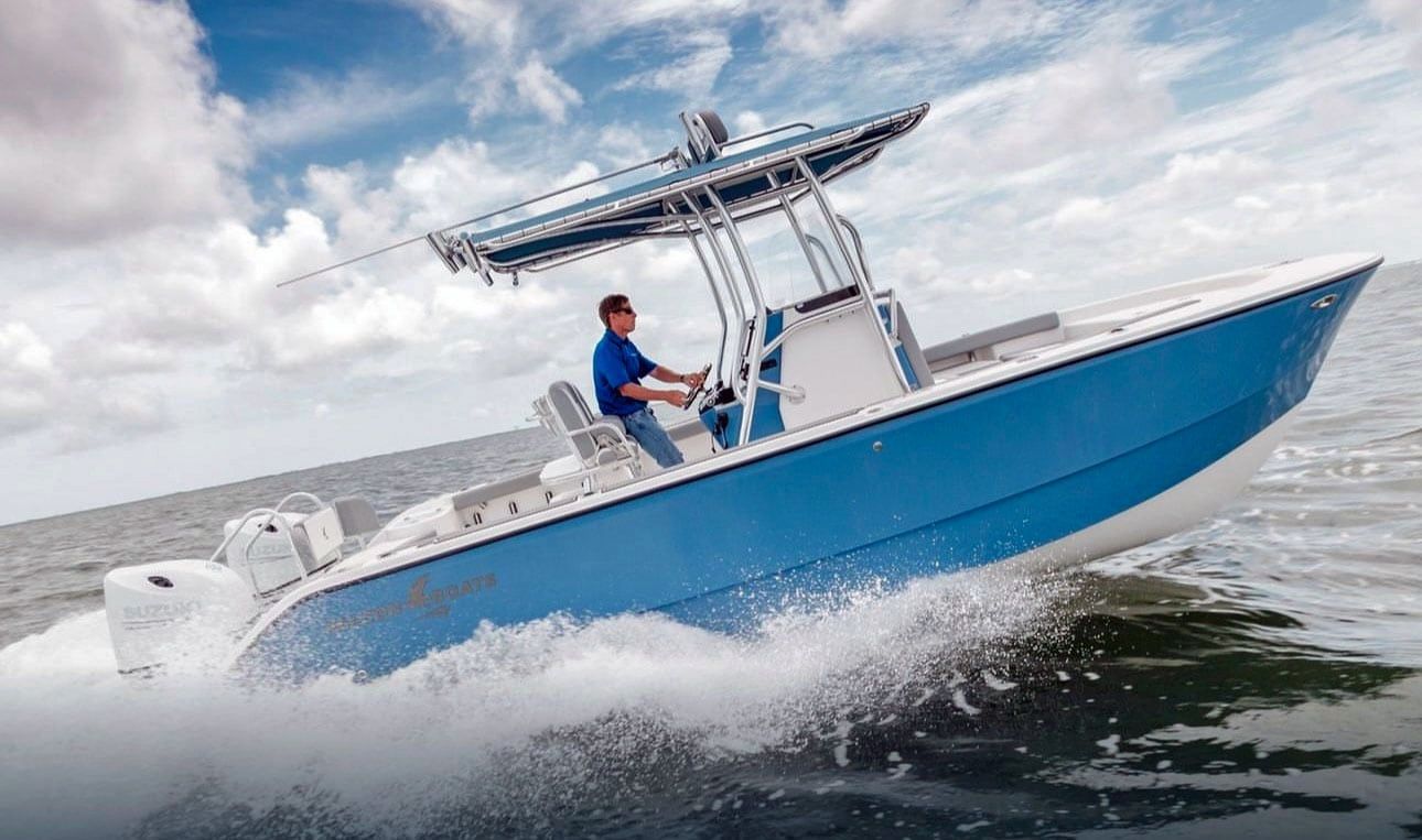 Blue and white motorboat speeding across the water with a man steering. Bright sky with clouds in the background.