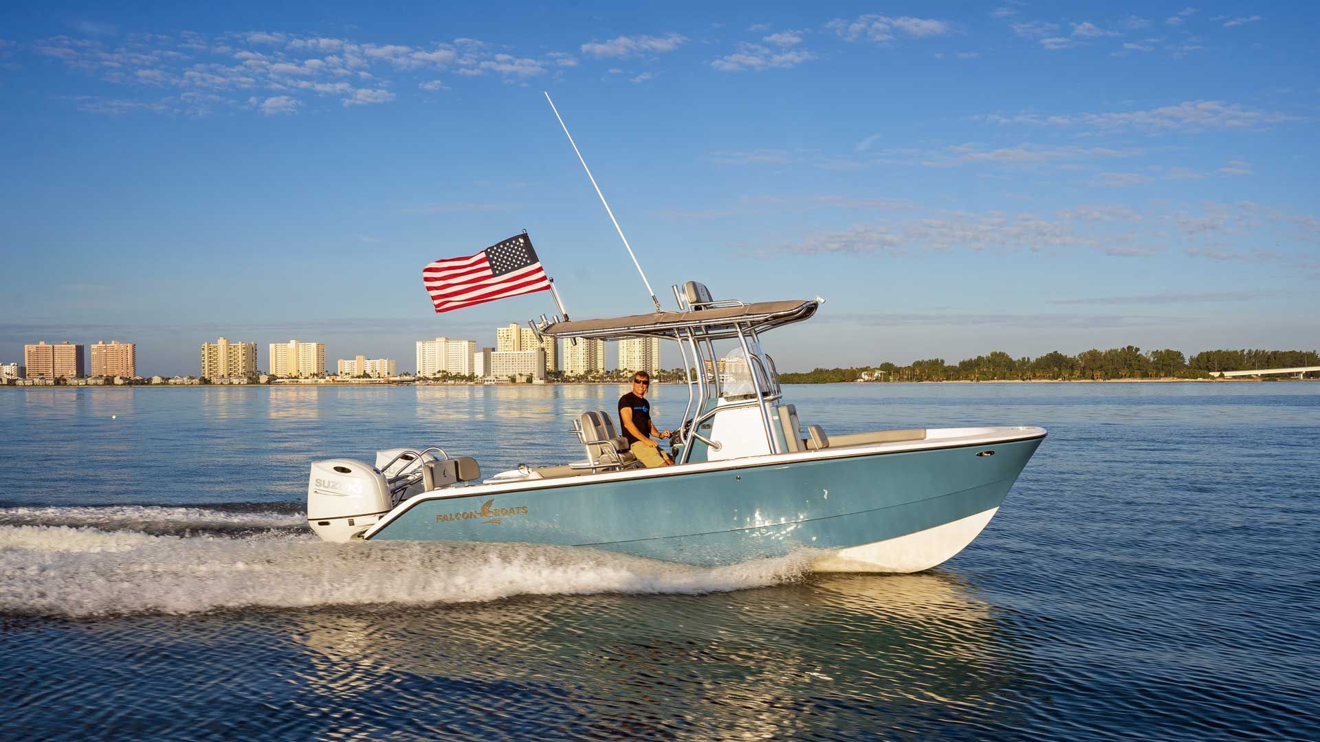 A blue and white motorboat with an American flag sails on the water, with a city skyline in the background.