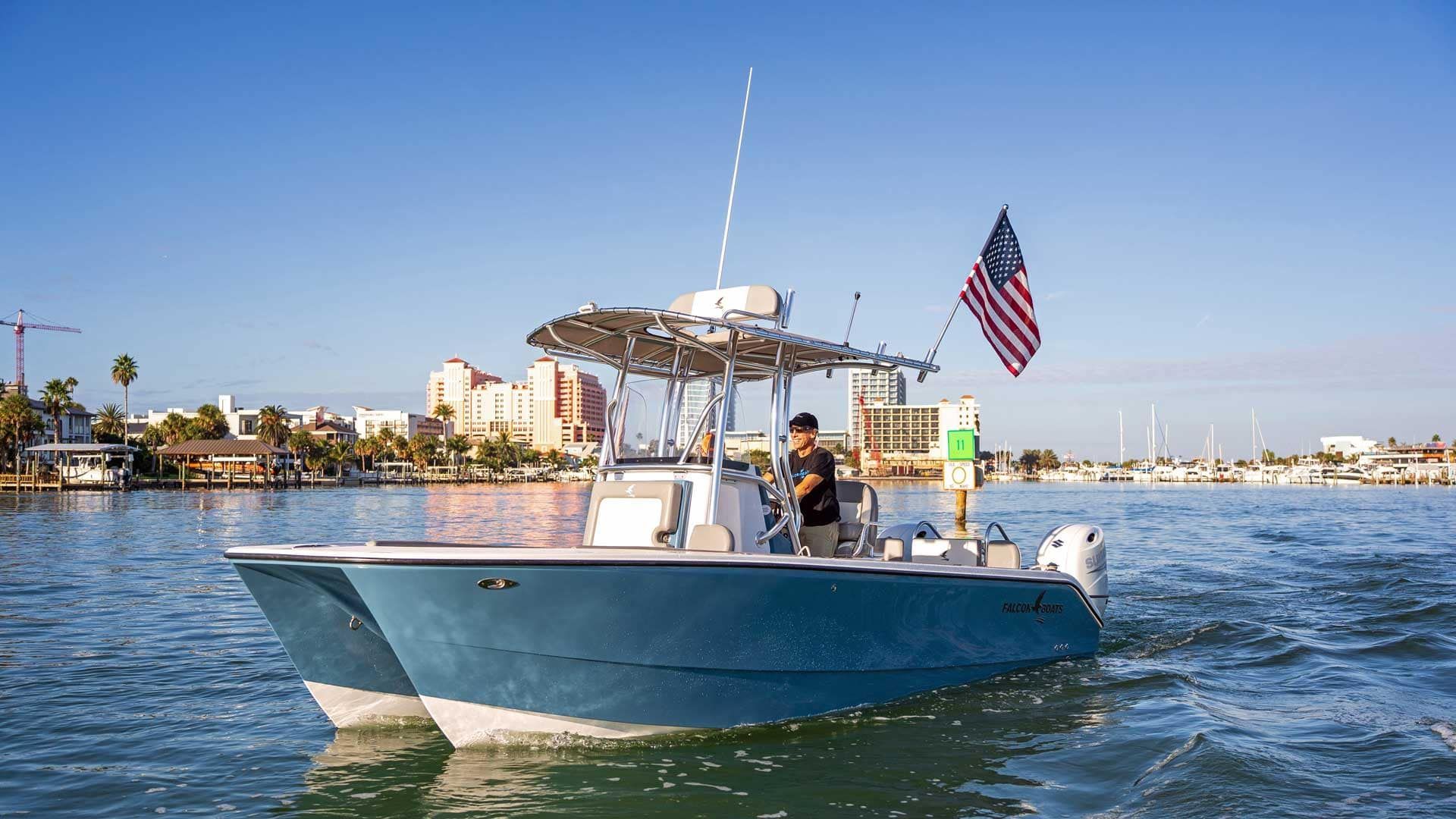 Blue motorboat on water with American flag, person at the helm, sunny day at a marina.
