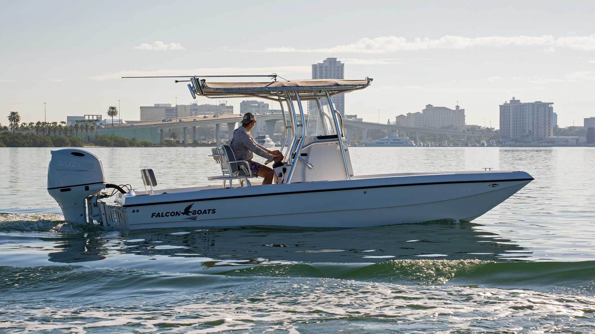 White center console boat with a person at the helm, moving on water with a city skyline in the background.