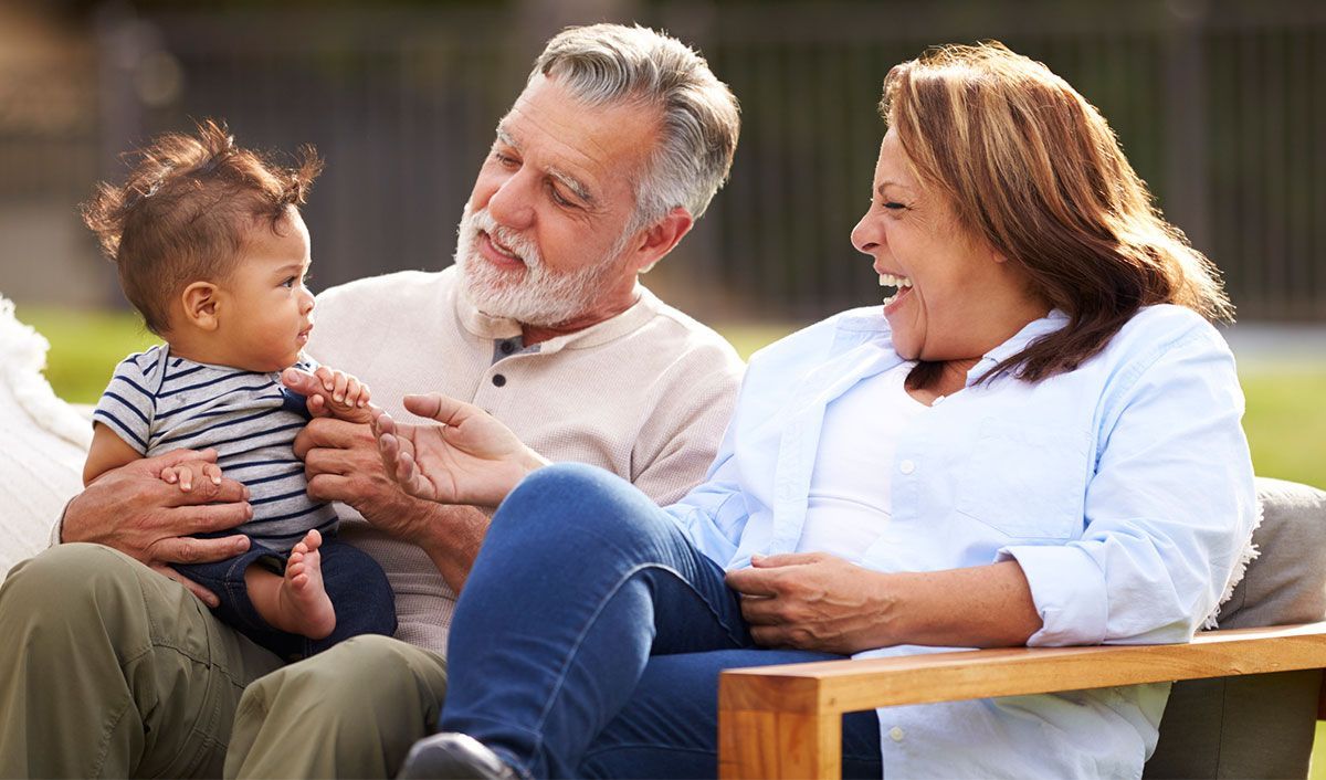Hispanic grandma and grandpa smiling at their grandchild outside on a park bench