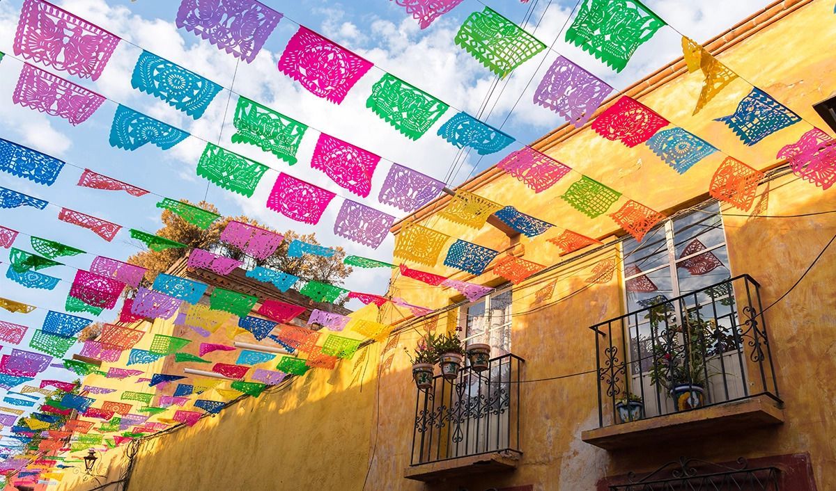 Apartment windows with plant accents underneath a canopy of vibrant papel picado Mexican paper decorations.