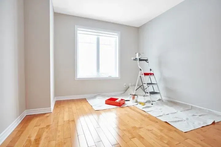 Freshly painted empty room with hardwood floors and painting gear.