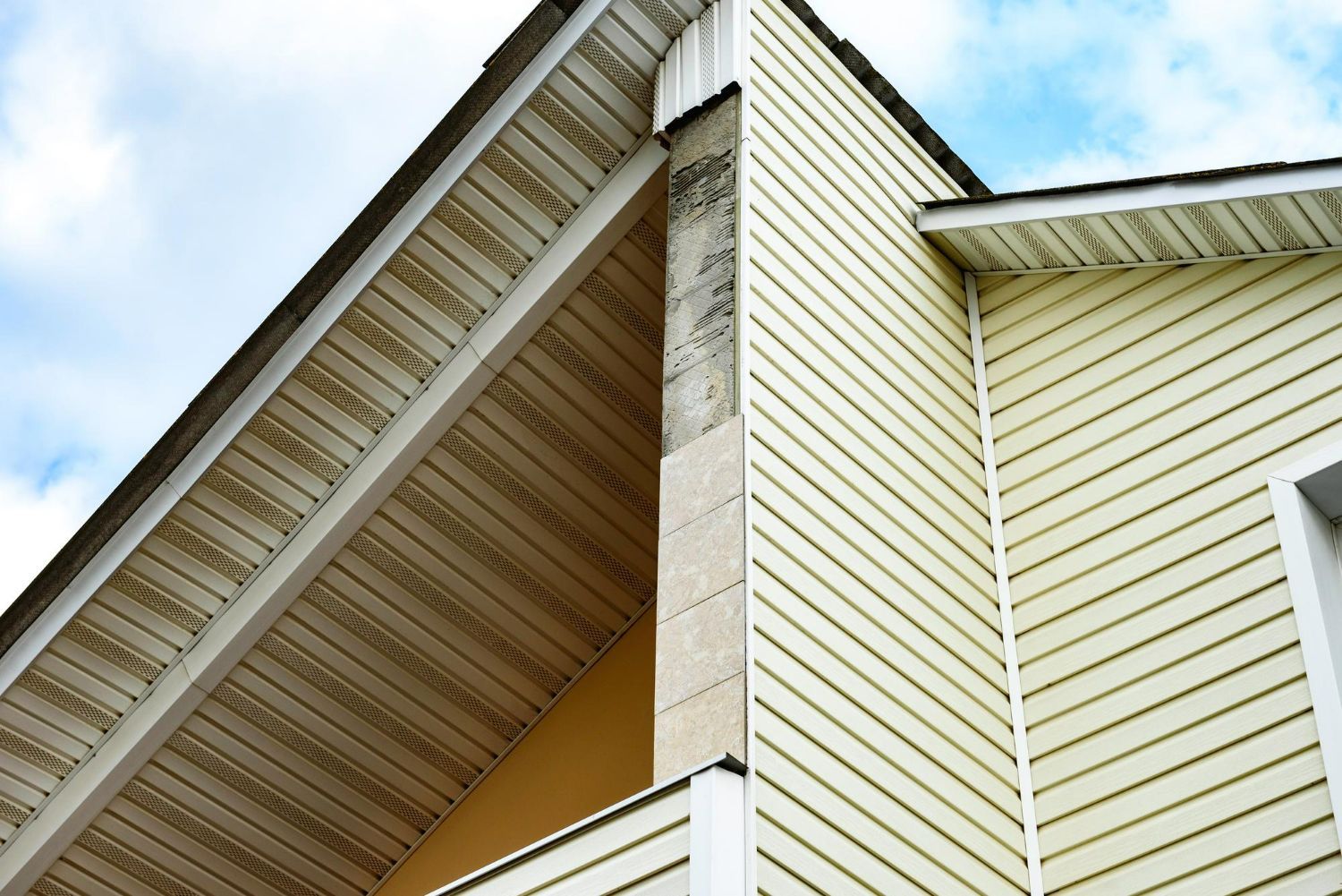 Beige vinyl siding on a house corner with a roof overhang and visible sky.