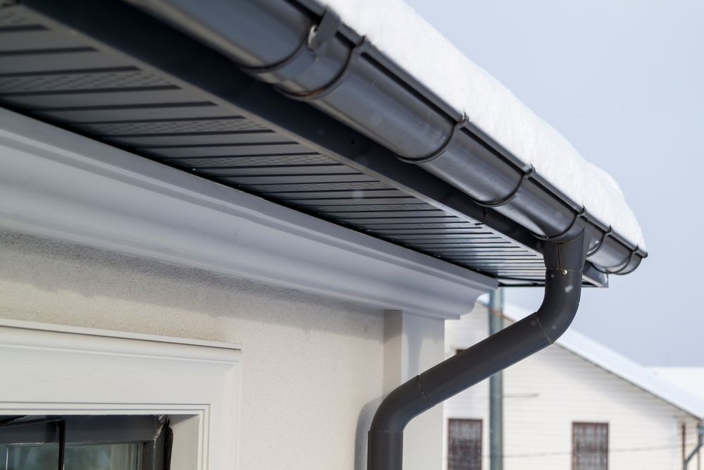 Black rain gutters with snow, attached to a white building.