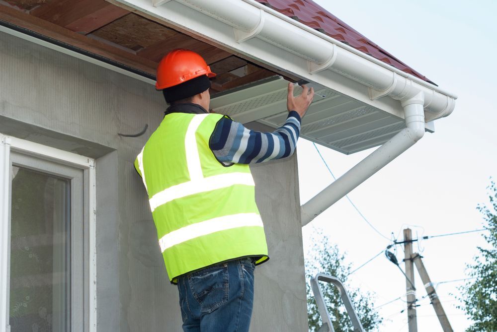 A man is standing on a ladder fixing a gutter on a house.