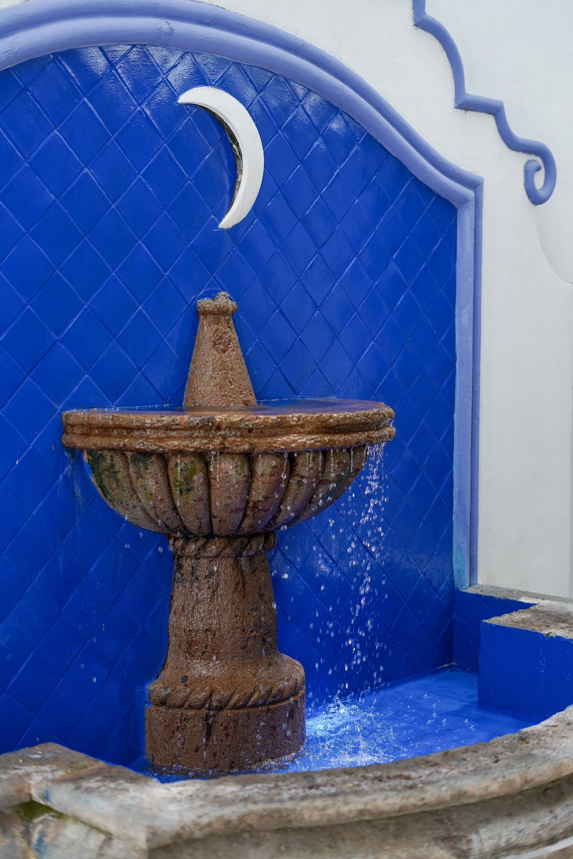 Water fountain with blue tiled background and crescent moon accent. Water cascading into the fountain basin.