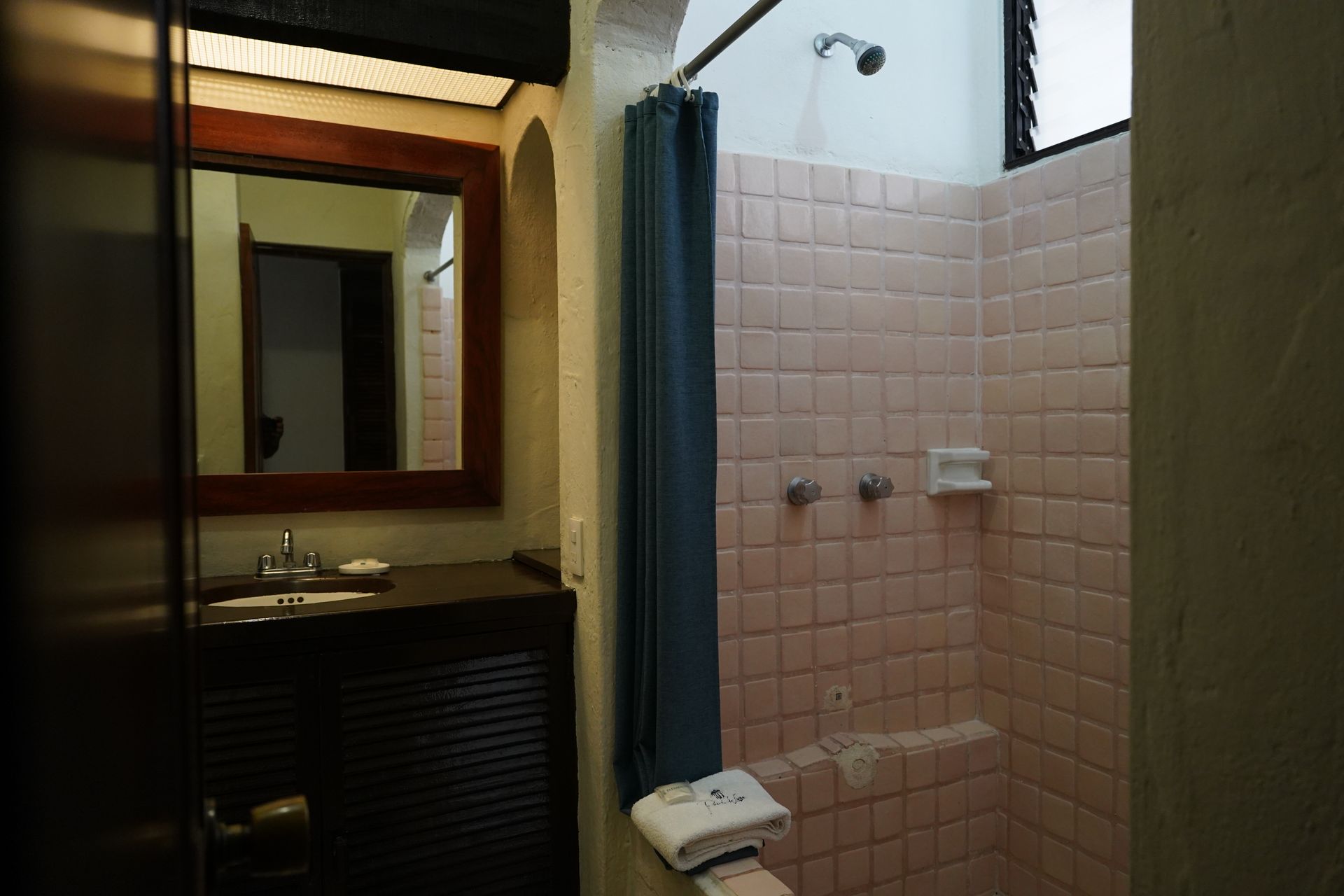 Bathroom with pink tiled shower, teal curtain, dark cabinet with sink, and mirror.