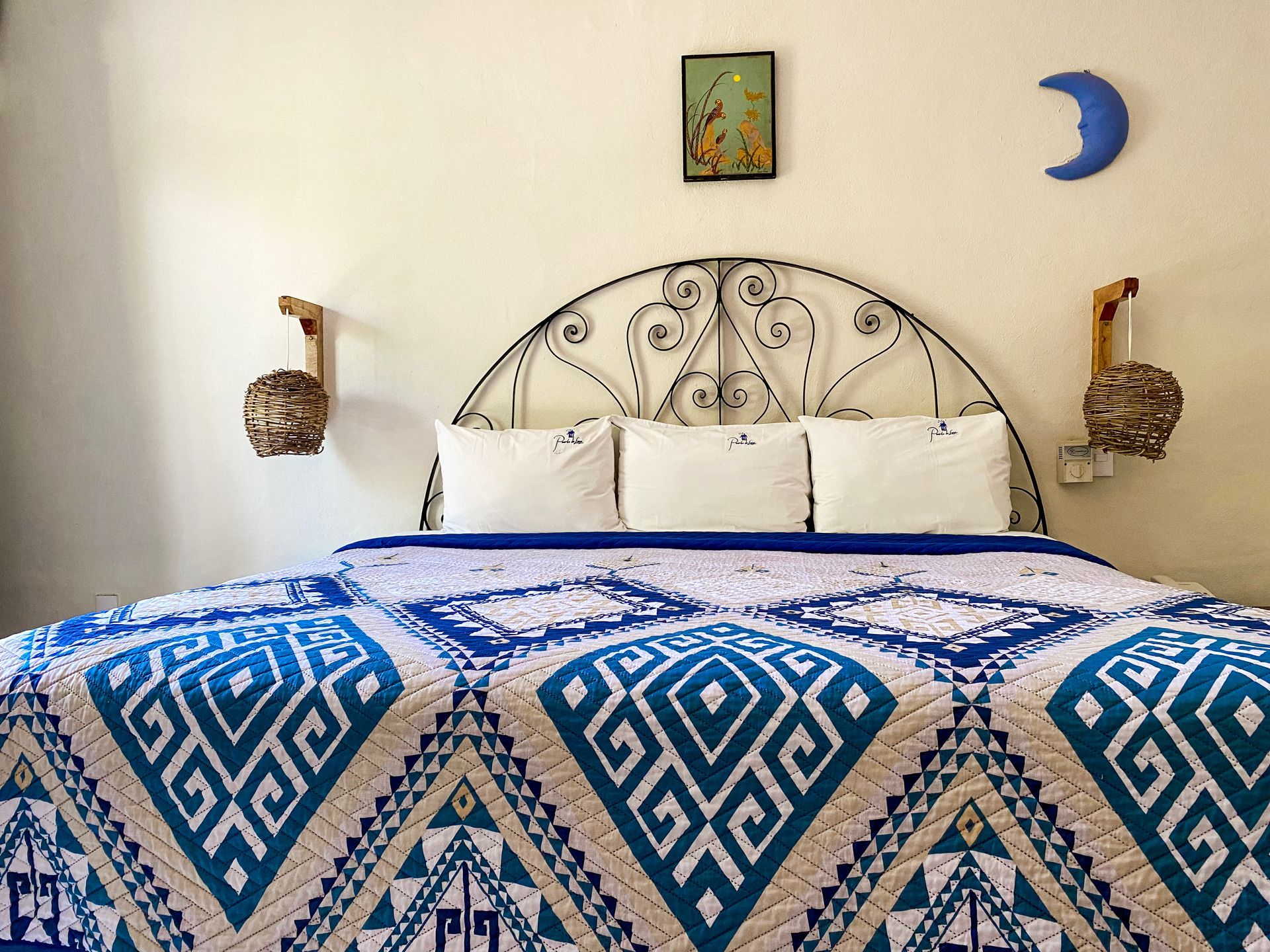 Bedroom with a blue and white patterned quilt, decorative headboard, and wall art.