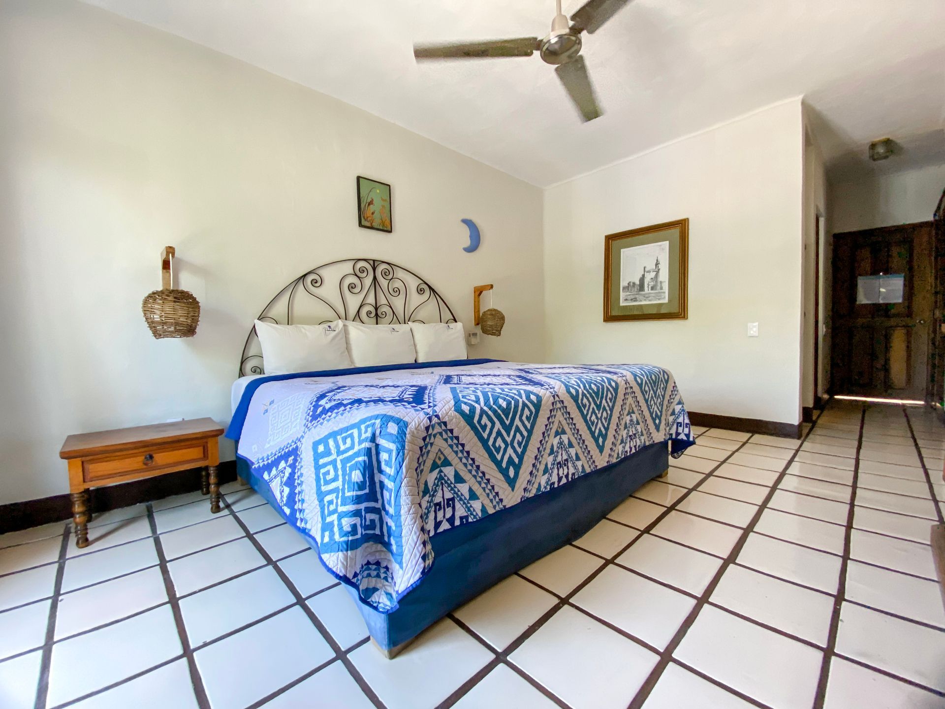 Bedroom with a king bed, blue patterned blanket, nightstand, ceiling fan, and tile floor.