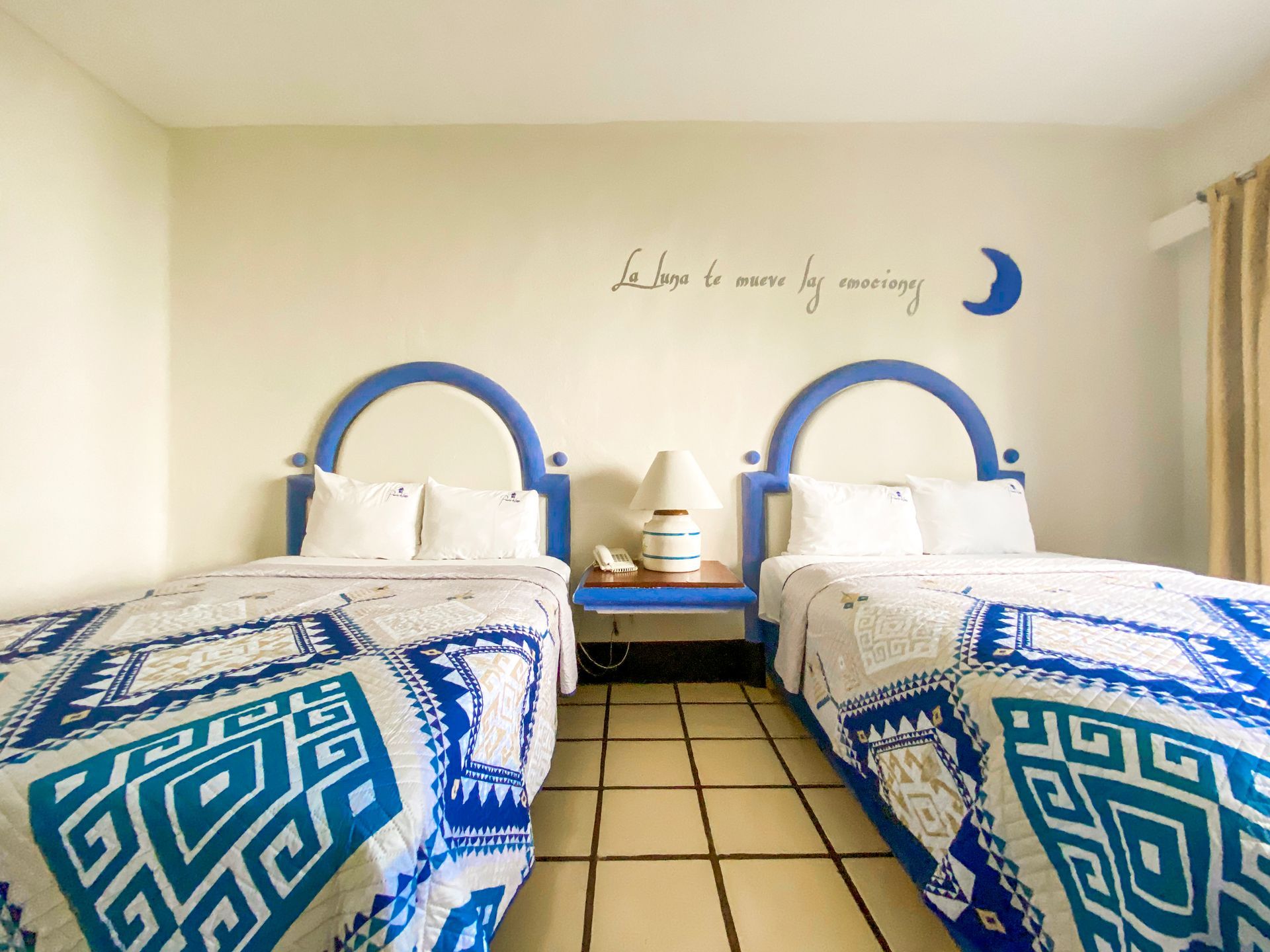 Two twin beds with blue accents in a room. A nightstand with a lamp sits between them.