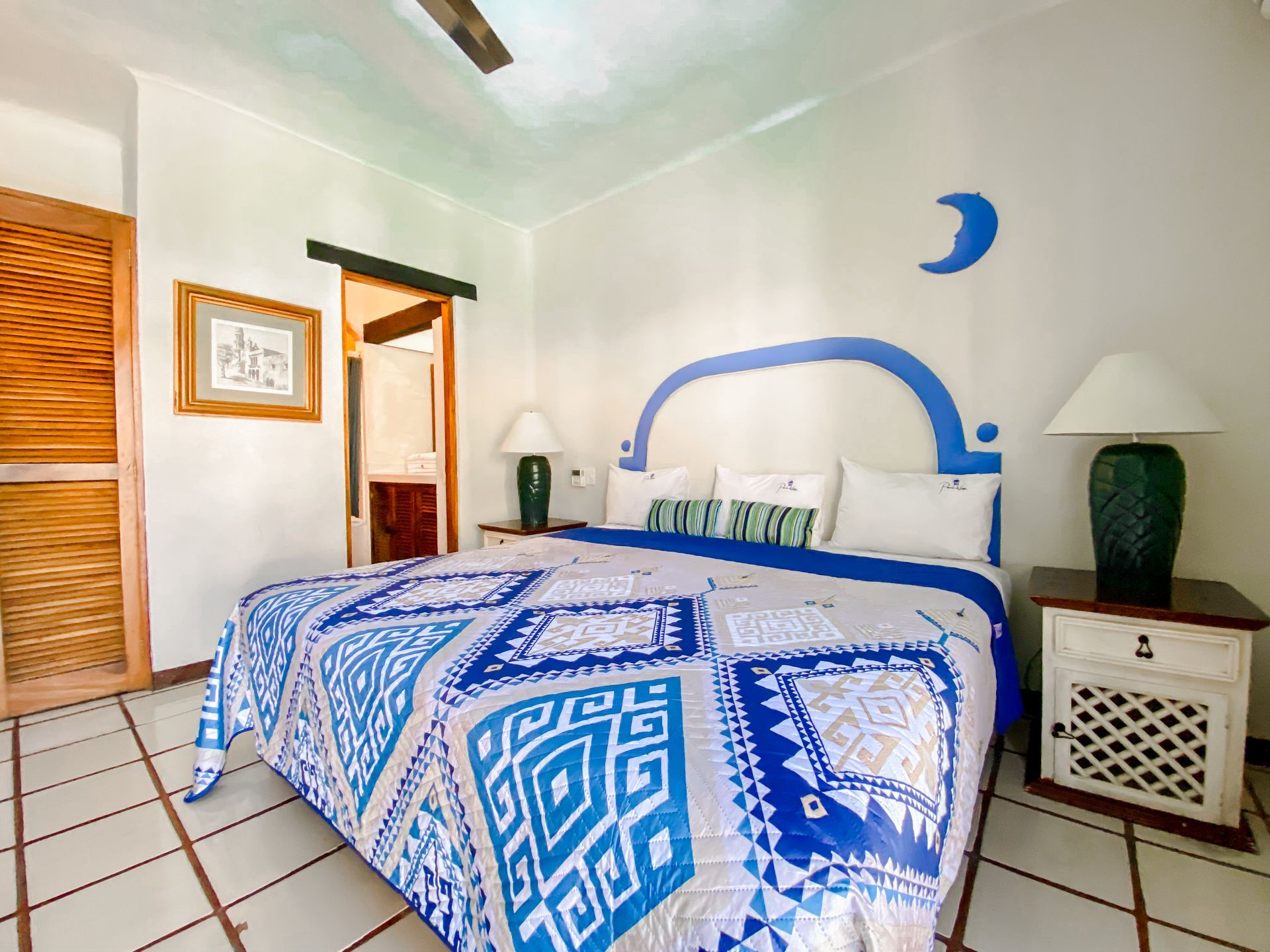 Bedroom with blue and white accents, bed, nightstands, and a door to the bathroom.
