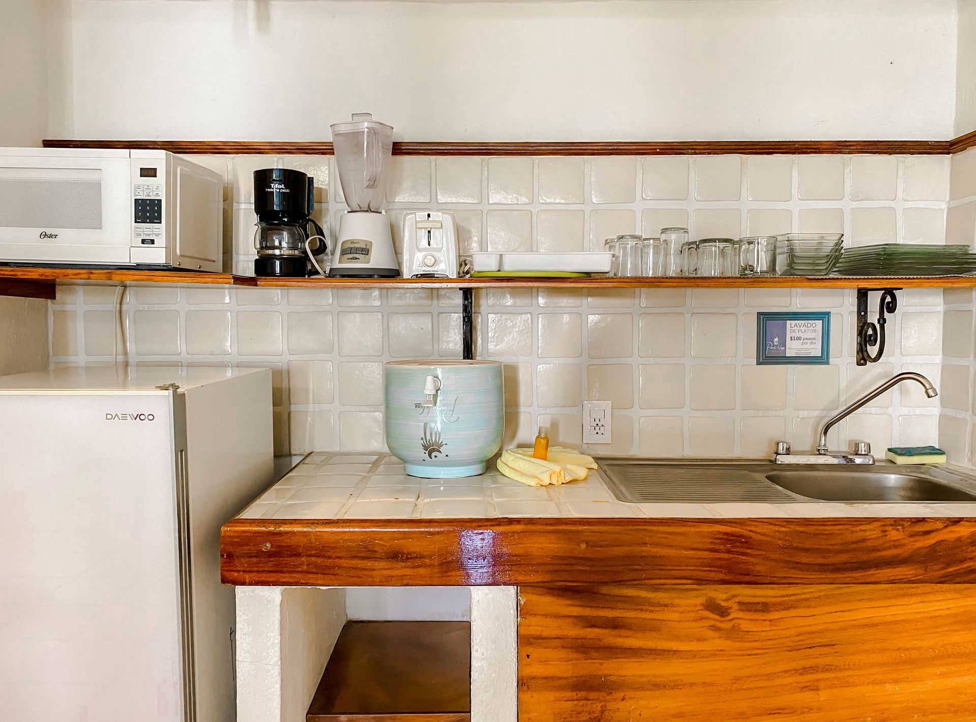 Small kitchen with a microwave, coffee maker, blender, sink, and shelves with dishes.