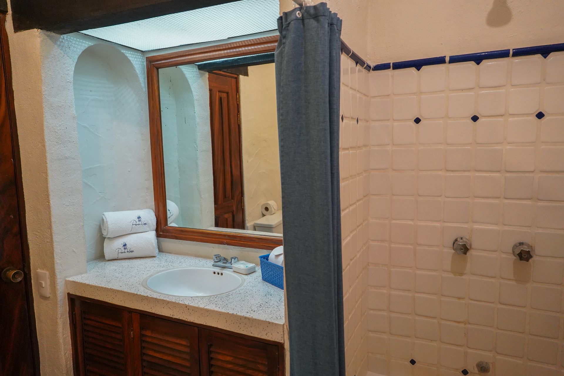 Bathroom with white tiled shower, sink with mirror, and blue shower curtain.