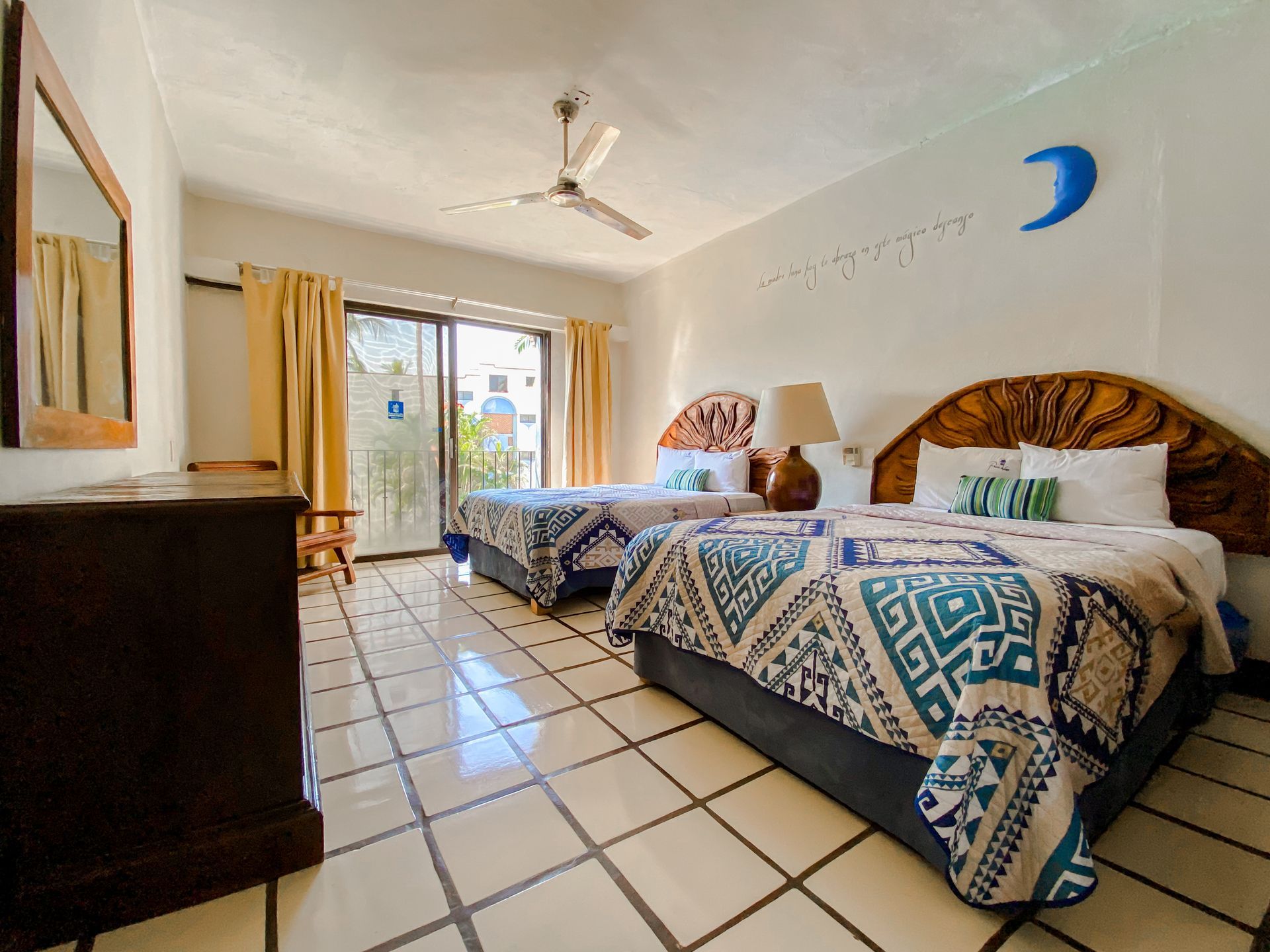 Bedroom with two beds, sliding door, beige curtains, dark wood furniture, and a ceiling fan.