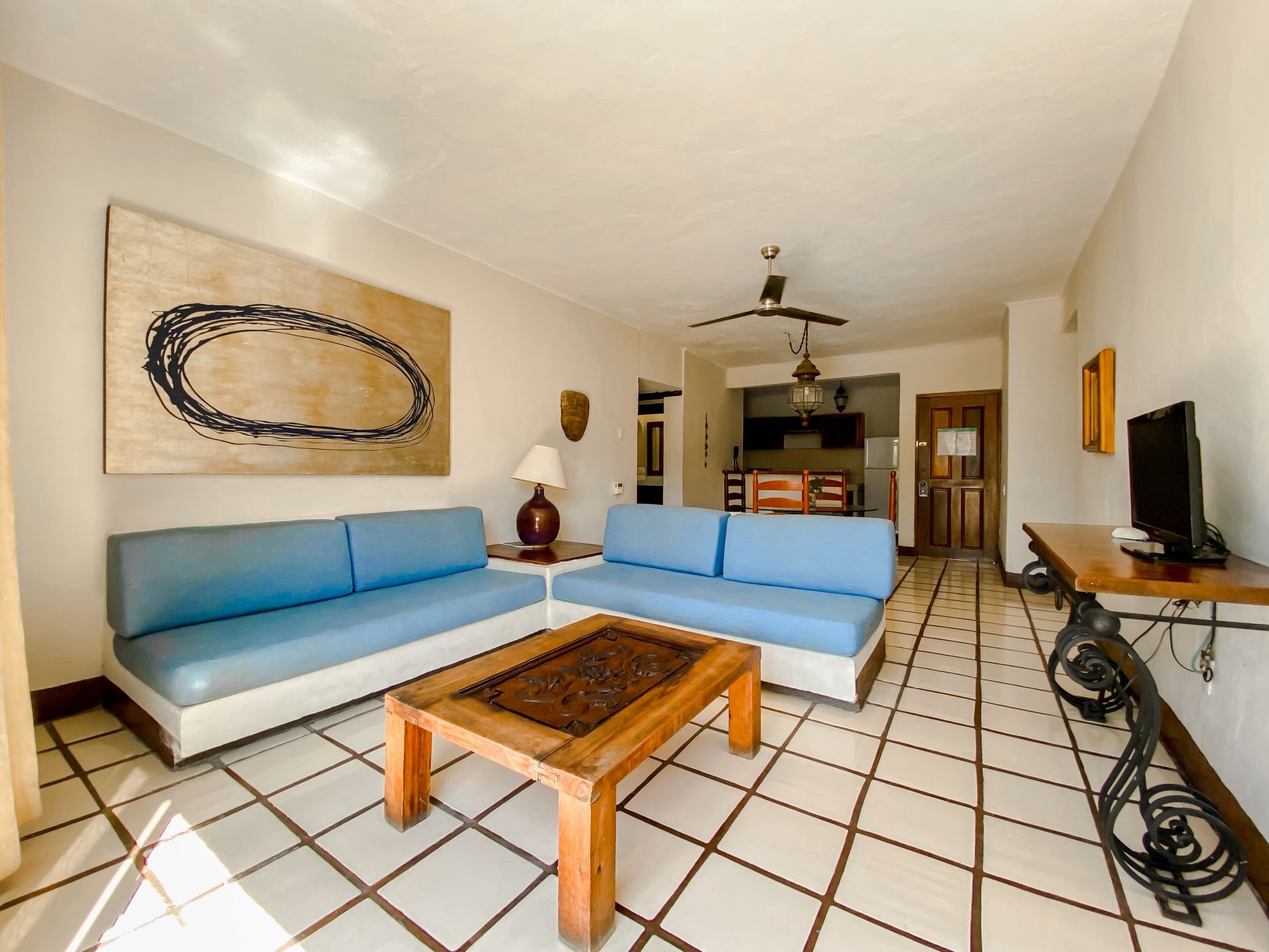 Living room with light blue sofas, wooden coffee table, and large artwork on white tile floor.