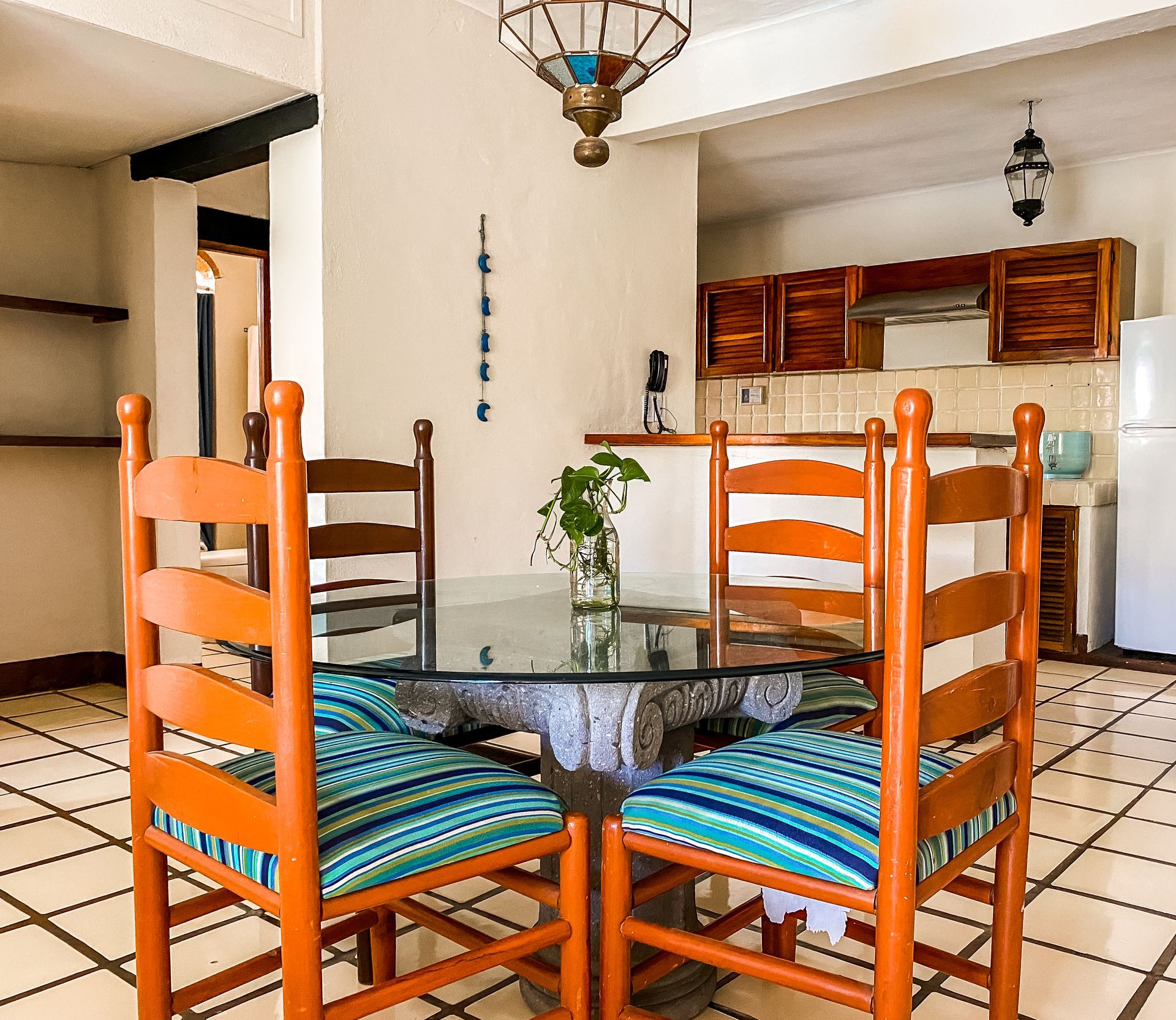 Dining room with wooden chairs, glass table, and kitchen in background.