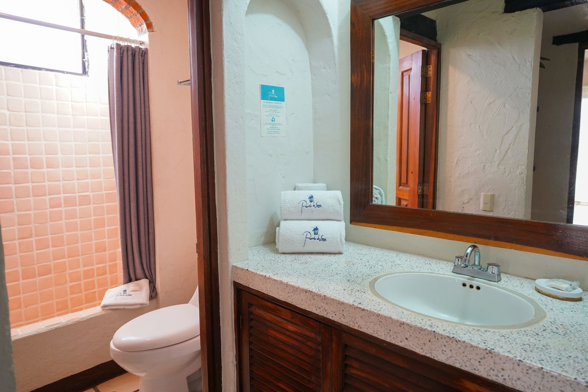 Bathroom with a shower, toilet, sink, and mirror. White walls, wood cabinet, and stacked towels.