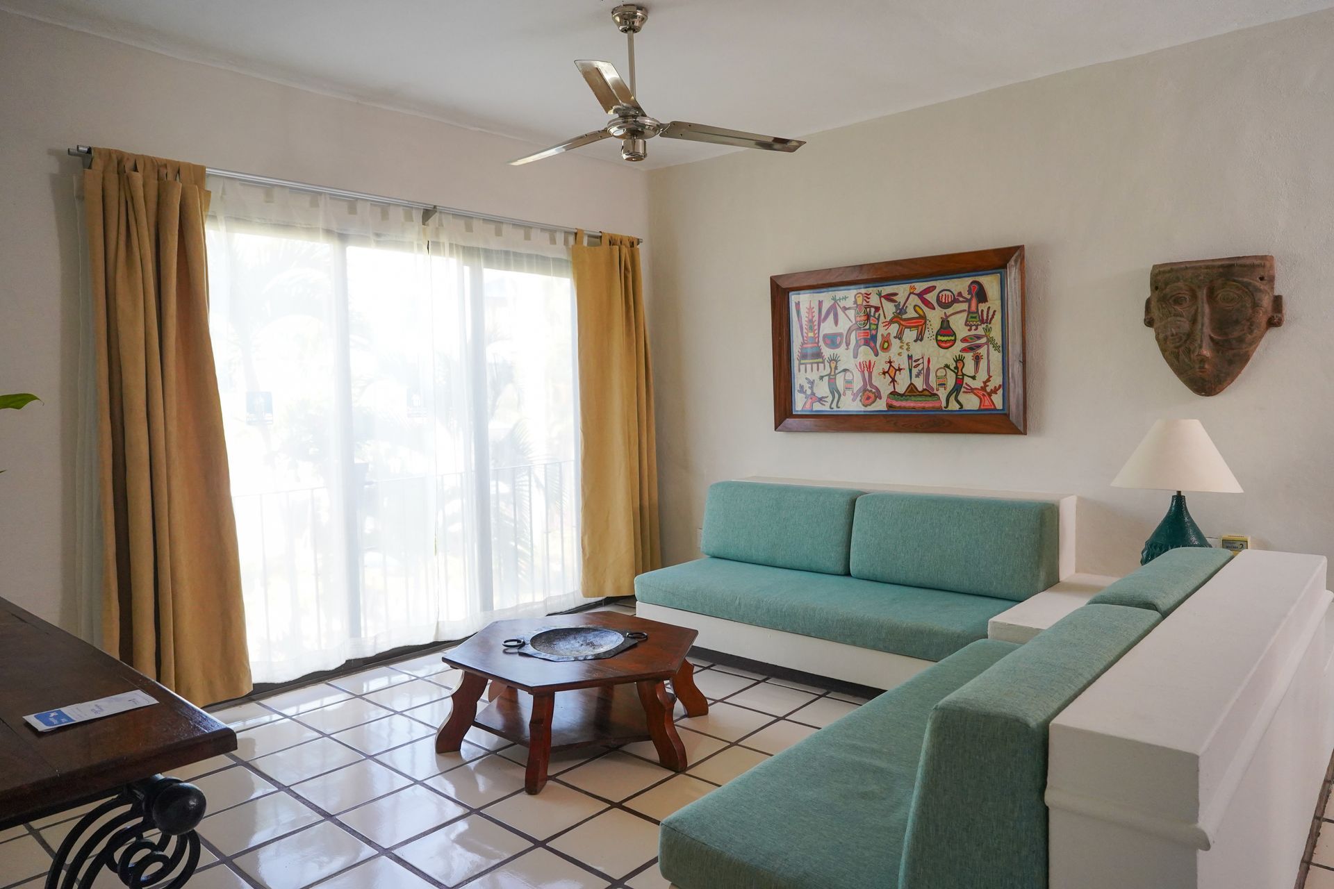 Man sitting on a teal couch, working on a laptop in a bright living room with a balcony.