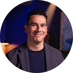 Man in a blue jacket smiles, looking upward. Background includes colorful artwork.