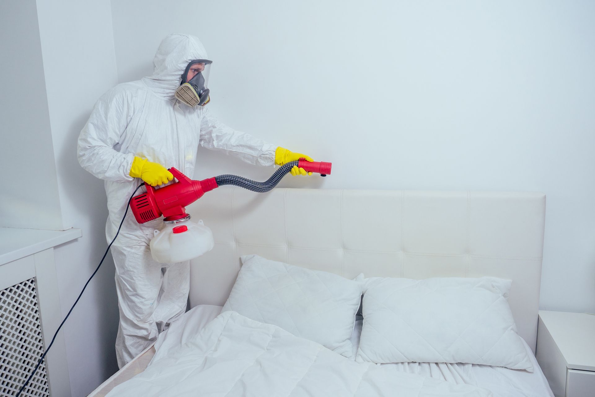 Pest control worker spraying pesticides in a bedroom. Pest control worker spraying pesticides in a bedroom.