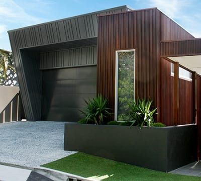 A modern house with a black garage door and a planter in front of it.