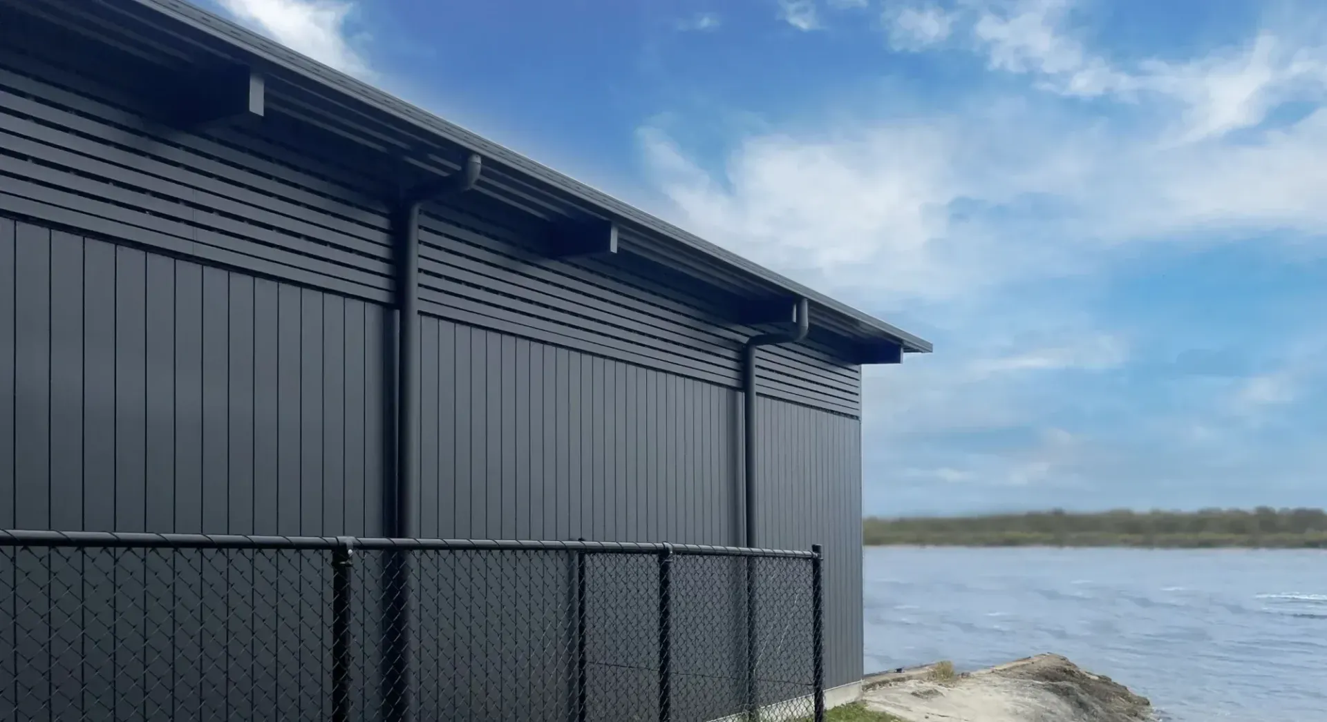 A black building with a chain link fence next to a body of water.