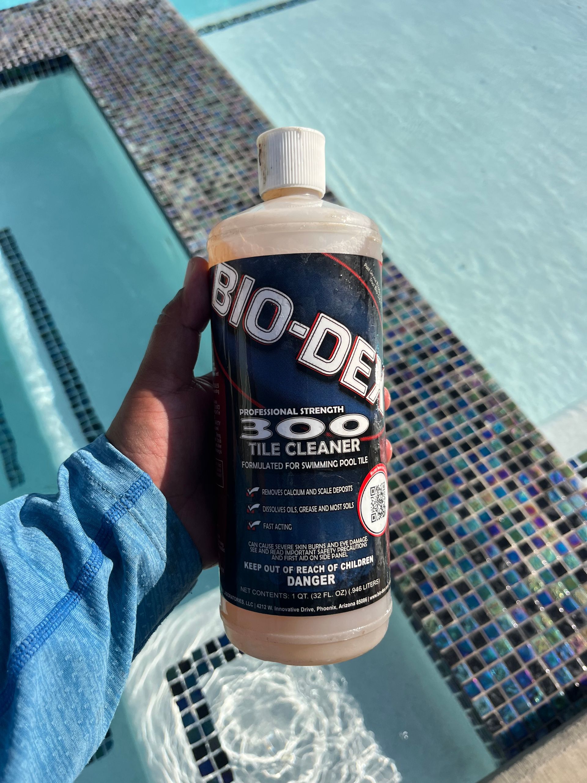 Hand holding a bottle of Bio-Dex 300 tile cleaner by a pool.