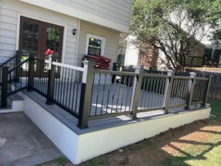 A large deck with a black and white railing is in front of a house.