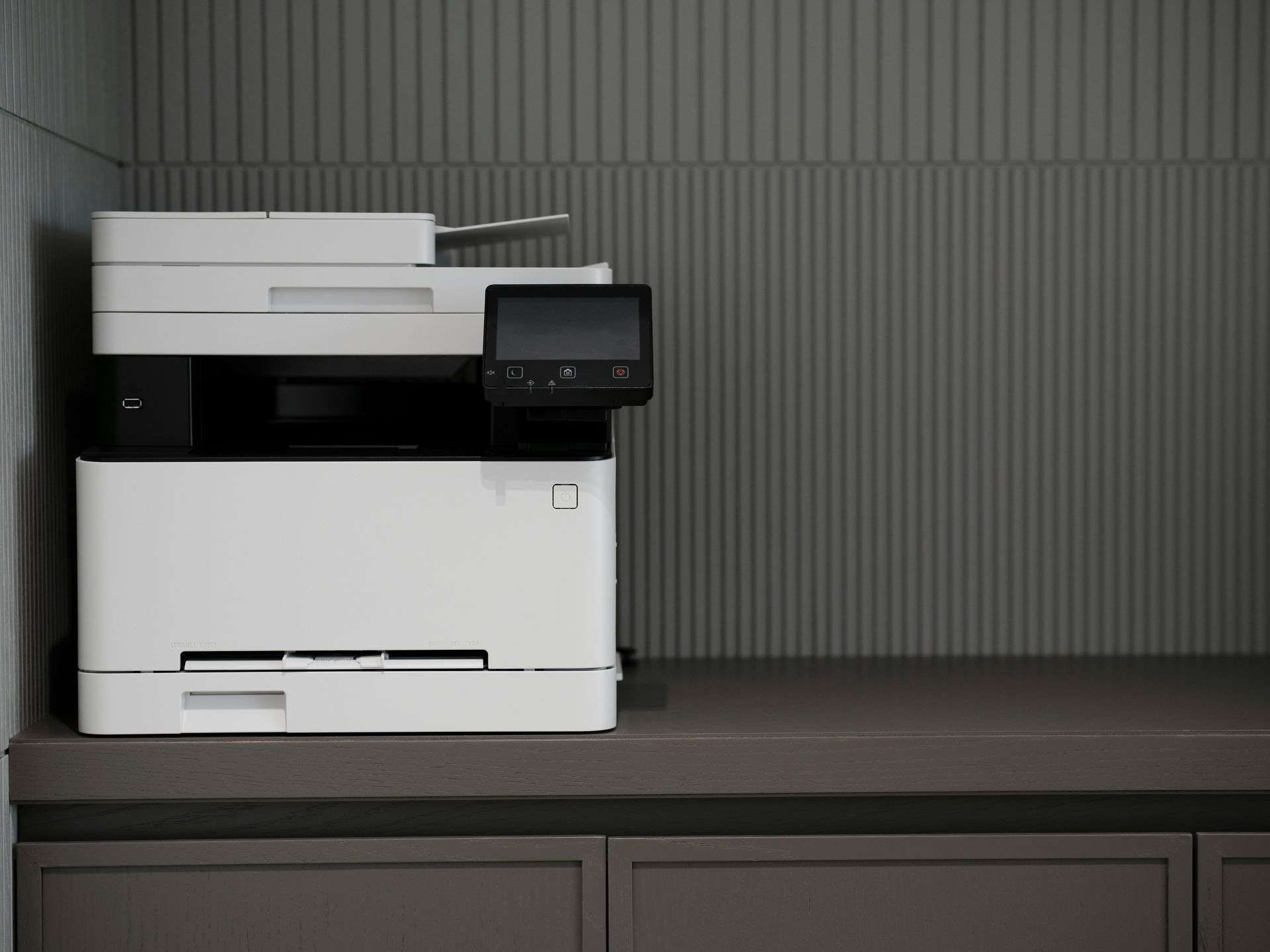 White office printer on a dark cabinet against a gray wall