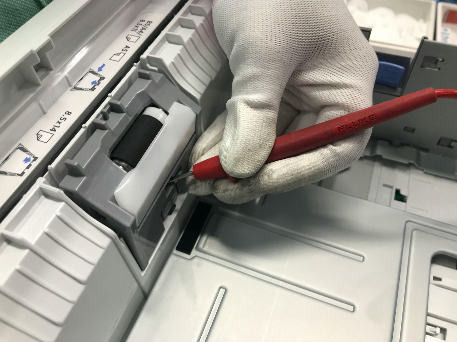 Gloved hand using a red stylus inside a gray copier tray