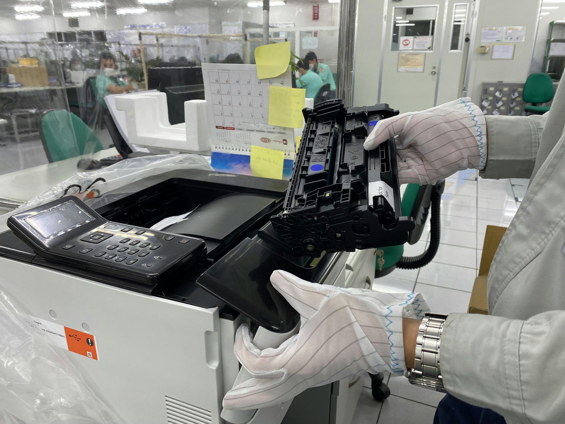 Gloved worker inspecting wiring inside a white electronic device in a factory lab