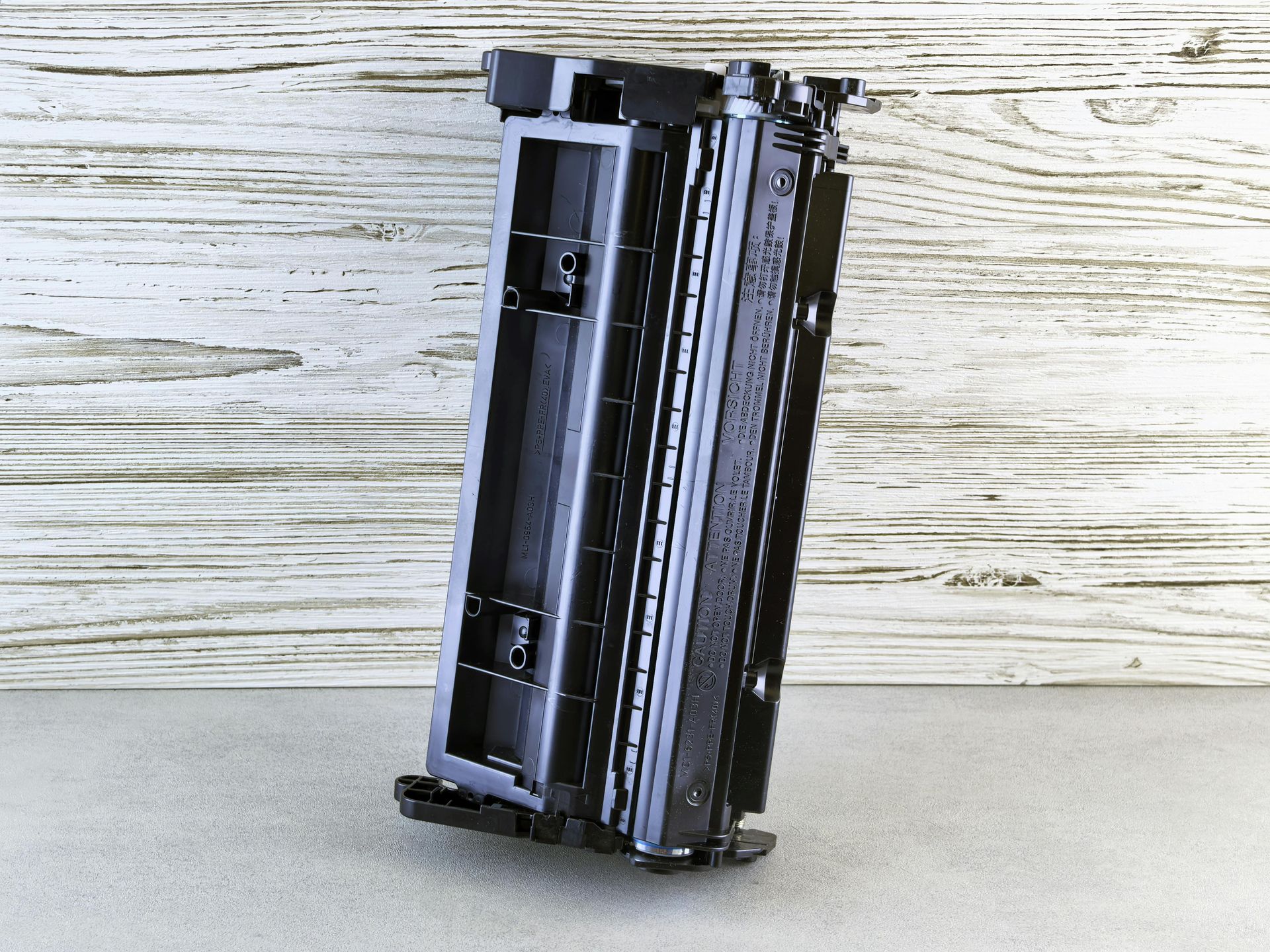 Black printer toner cartridge standing upright on a light wooden surface.