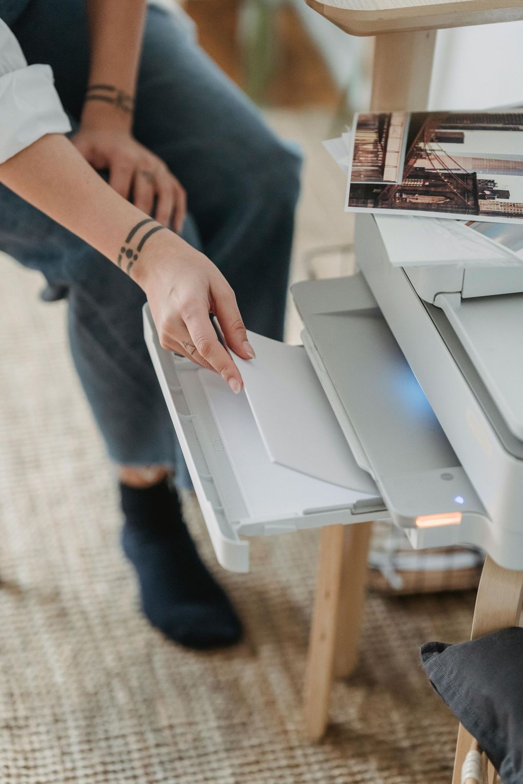 Person loading paper into a printer beside a desk and laptop