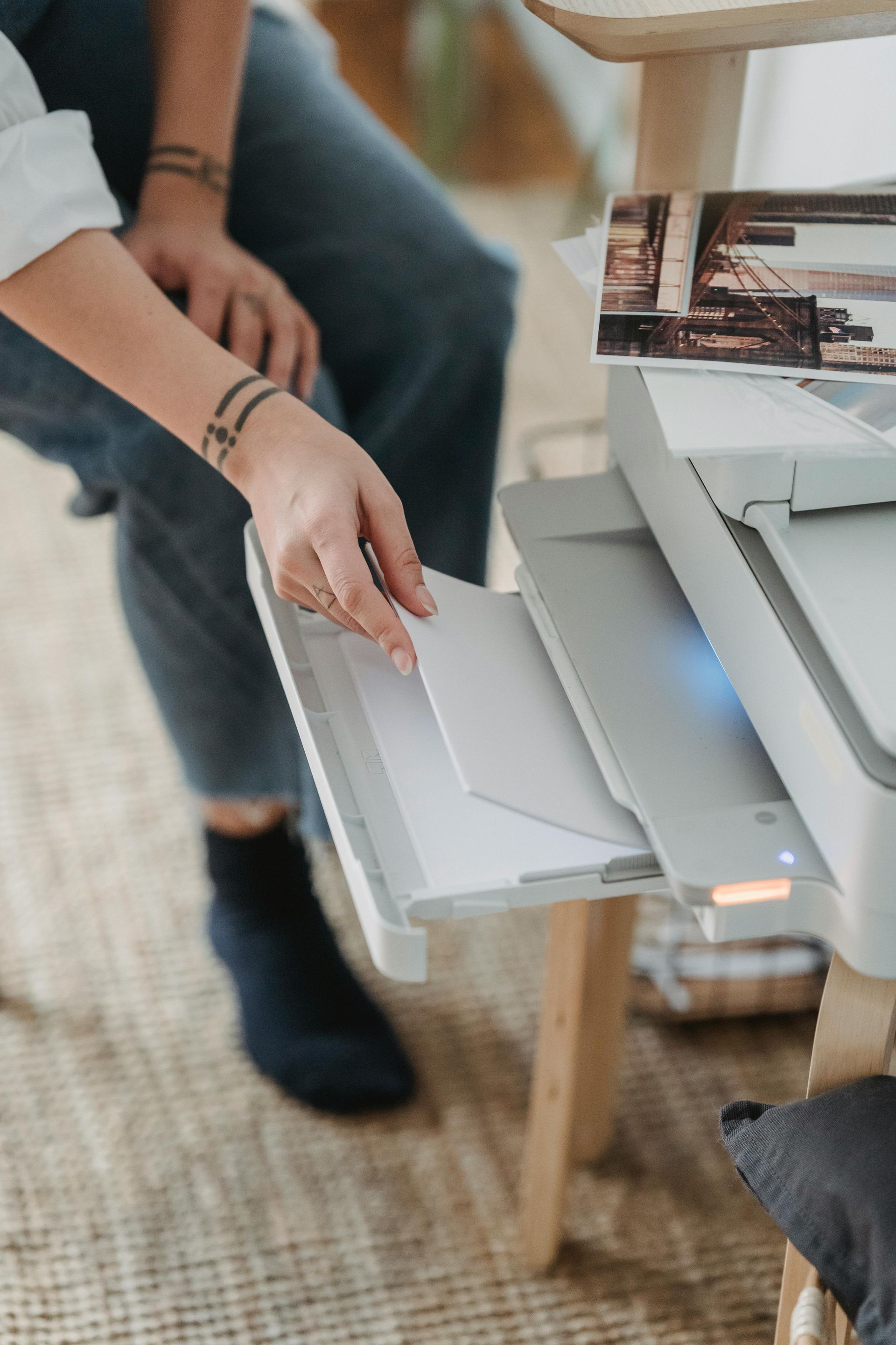 Hand inserting a sheet into a printer tray beside a desk and laptop