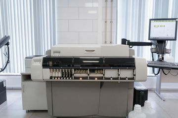 Automated lab analyzer in a bright clinical laboratory with a monitor and equipment cart
