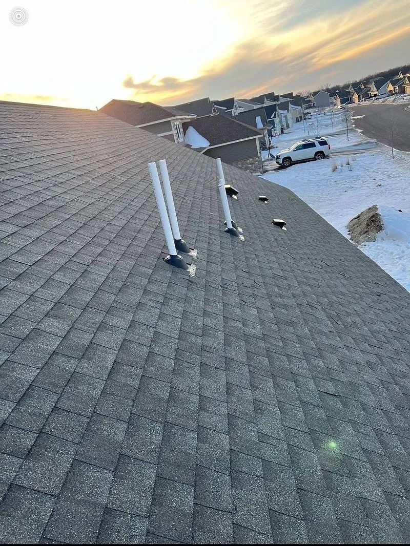 Rooftop view with vents against a winter sky. Gray shingles, snow on the ground, and a vehicle visible in the distance.