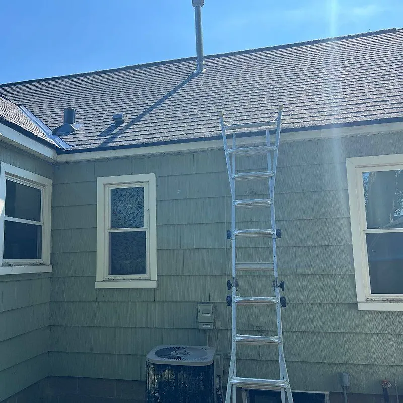 Ladder against a green house with a gutter system, clear sky above.