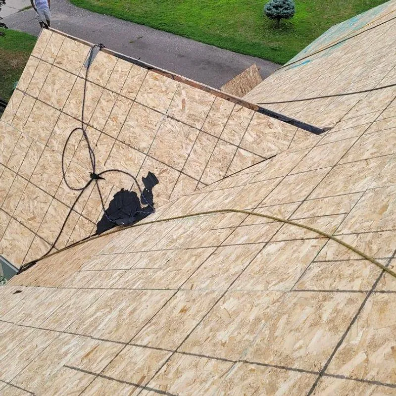 Roof in progress, plywood and electrical wiring visible, person standing on the roof.