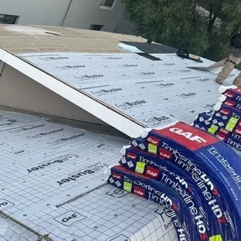Roofers installing shingles on a roof, stacks of GAF Timberline HD shingles visible.