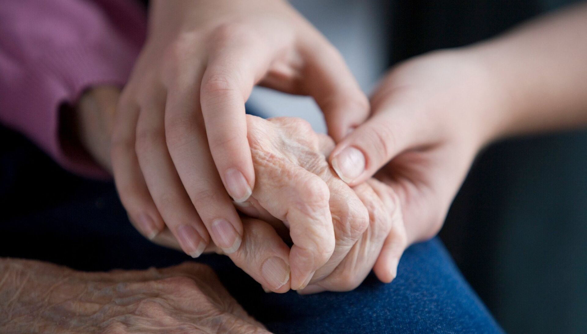 A young woman is holding the hand of an older woman.