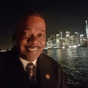 Man in suit smiles, night cityscape background with lights on water.
