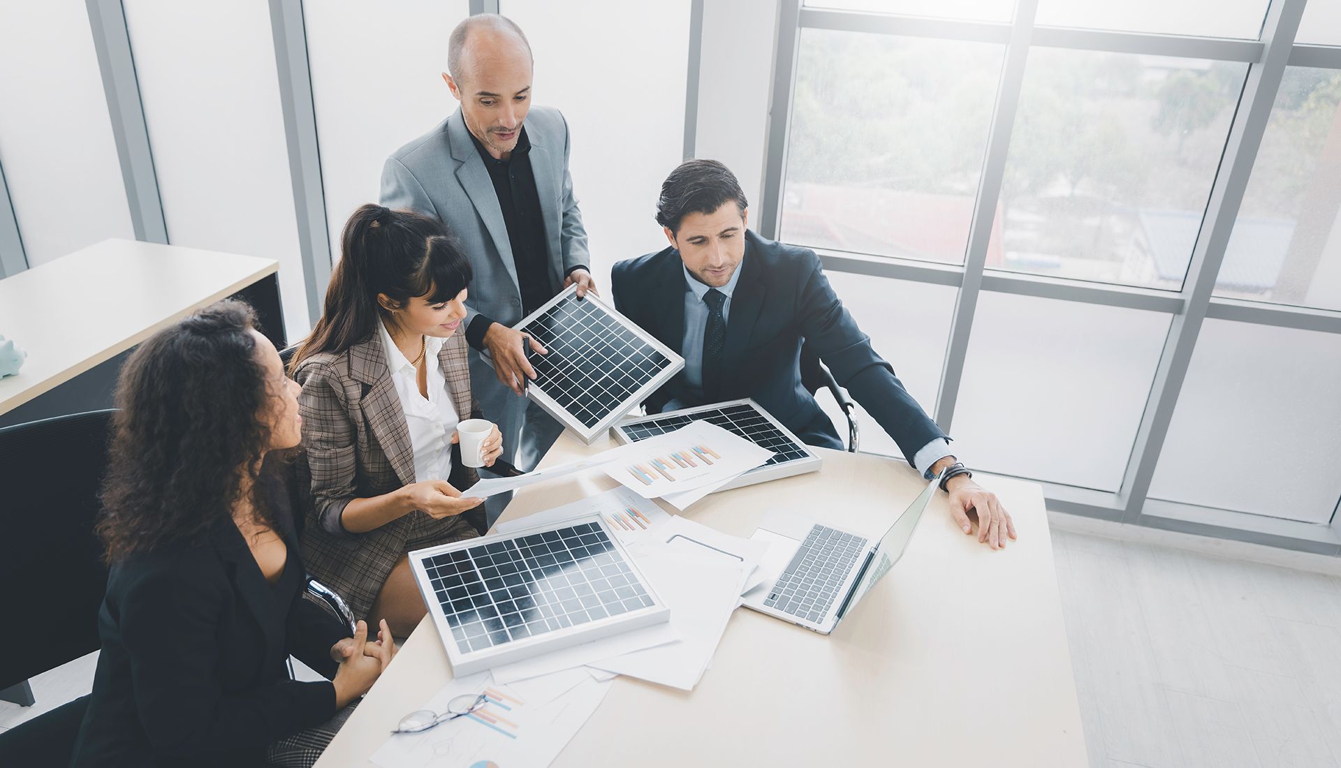 Business team reviews solar panel models in a sunny office.