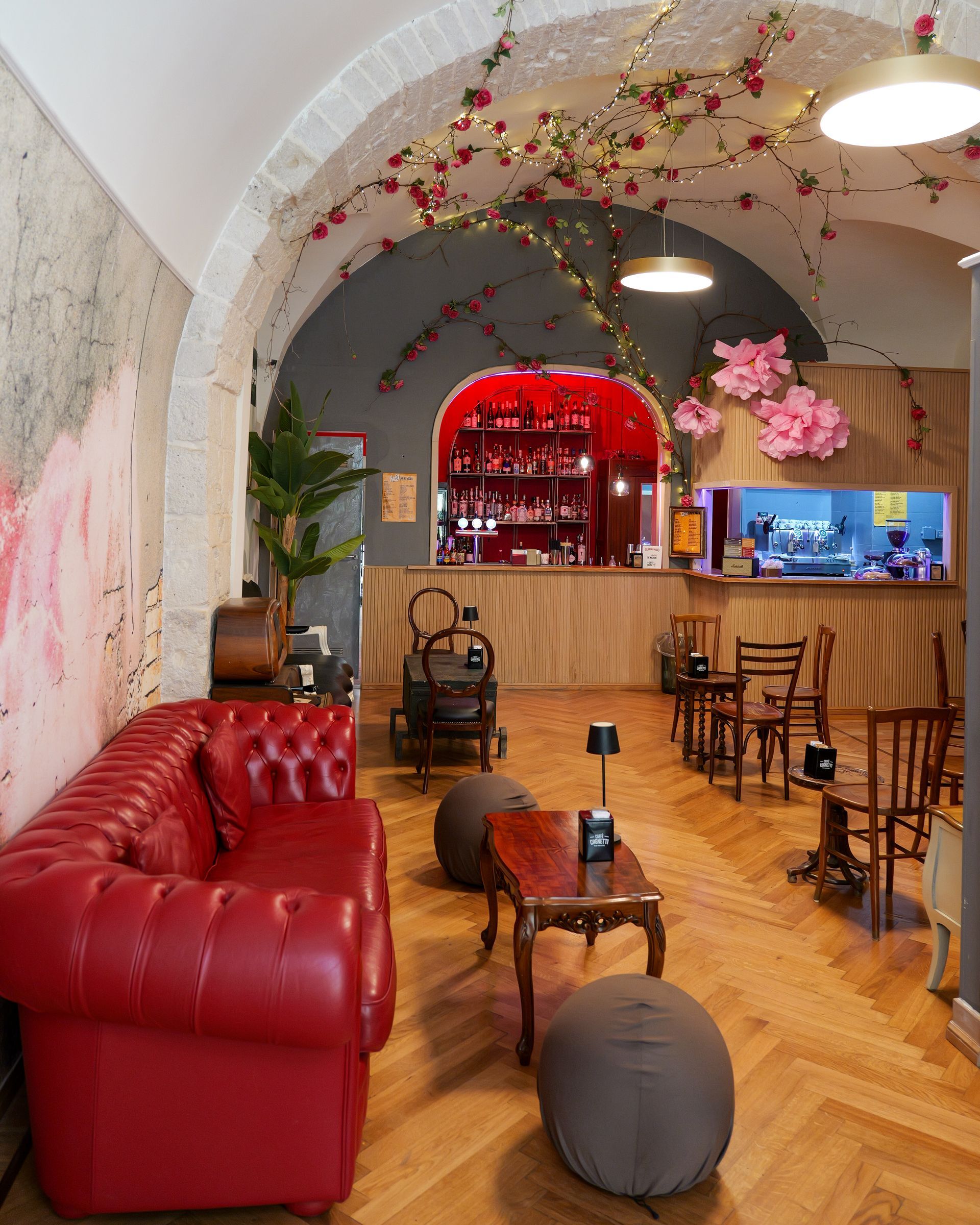 Divano rosso trapuntato in un bar con bancone rosso, pavimenti in legno e decorazioni floreali.